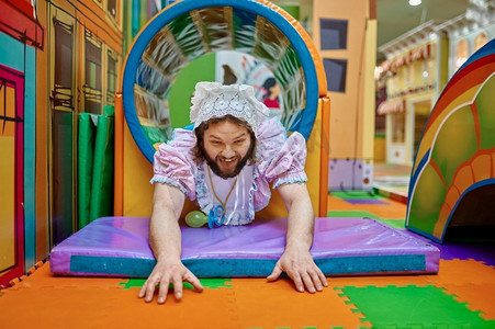 搞笑的男人穿着像新生儿一样在儿童日托中心的迷宫中玩耍。好笑的男人像婴儿一样在迷宫中玩耍