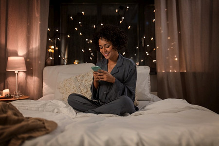 技术,就寝时间和休息概念-穿着睡衣的快乐微笑的女人,晚上坐在床上拿