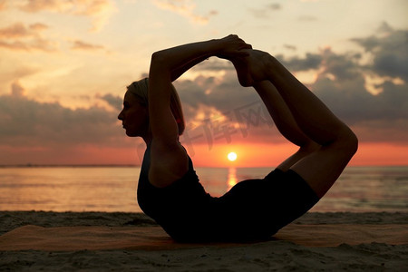 健身、运动和健康生活方式理念--日落后在海滩上做瑜伽鞠躬姿势的女性。日落后，一名女子在海滩上做瑜伽鞠躬姿势