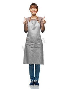 烹饪，烹饪和人的概念-快乐的微笑的女人在围裙上对白色背景竖起大拇指。围着围裙微笑的女人