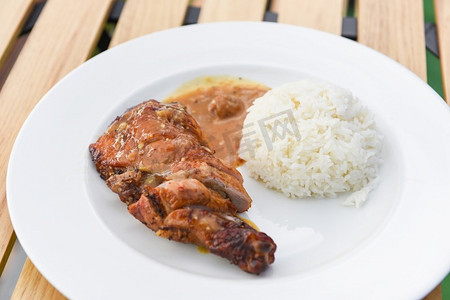 泰国饭食物，熟的白米饭和烤鸡有酱汁在白色盘子和木桌子背景，辛辣的烧烤鸡腿 