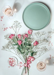 美学icon摄影照片_花束与粉红色玫瑰，空盘子和玫瑰酒在玻璃在阳光在白色背景。俯视图。美学平铺