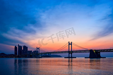 日出的广安桥上有摩天大楼和戏剧性的天空。韩国釜山。日出时分的广安桥。韩国釜山