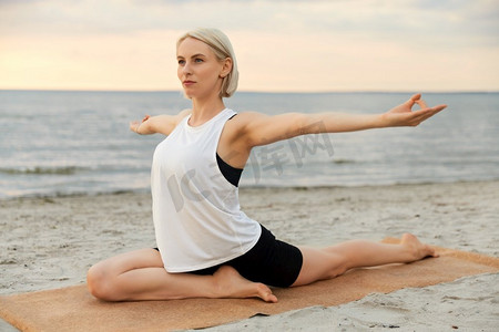 健身、运动和健康的生活方式概念—妇女做瑜伽鸽子姿势在海滩超过日落。妇女做瑜伽鸽子姿势在海滩