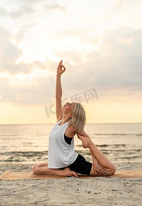健身、运动和健康的生活方式概念—妇女做瑜伽美人鱼姿势在日落的海滩。妇女做瑜伽美人鱼姿势在海滩