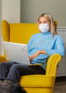 一名妇女戴着医用口罩在疫情期间在家工作笔记本电脑