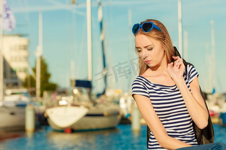 旅游休闲与人的理念。戴着蓝色心形太阳镜的时尚金发女孩在码头与港口的游艇对峙