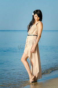 一个女孩与黑色的头发在一个米色的裙子在海岸的蓝色的大海