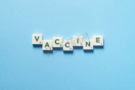 疫苗蓝色摄影照片_疫苗字是由拼写的瓷砖在蓝色背景上形成的。疾病预防和身体健康意识。由拼凑的瓷砖制成的疫苗。