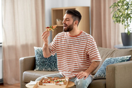 送餐、消费和人的概念—快乐的男人在家吃外卖披萨。快乐的男人在家里吃外卖披萨