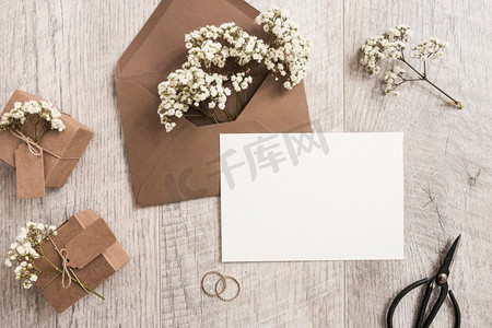 水果礼盒摄影照片_棕色信封，婴儿S口气，鲜花，礼盒，结婚戒指，剪刀，白色卡片，木质背景