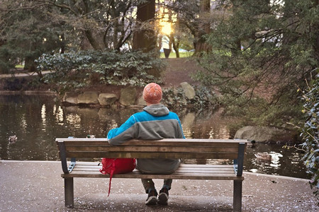一个男人独自坐在美丽的春天公园树间的长凳上。 