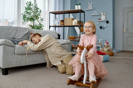 疲倦的疲劳父亲睡在地板上和可爱的顽皮女孩在家里玩。疲惫的疲劳父亲和顽皮的女孩