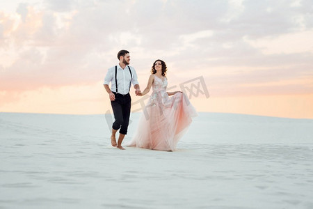 一对年轻的夫妇，一个穿着黑色裤子的男孩和一个穿着粉红色裙子的女孩正沿着沙漠的白色沙滩走着