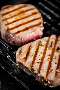 金枪鱼摄影照片_烤盘里的金枪鱼牛排。在黑色背景上。高质量的照片。烤盘里的金枪鱼牛排。