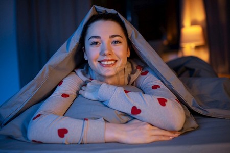 人，就寝时间和休息概念—快乐的少女躺在毯子下在床上在家里晚上。快乐的十几岁的女孩躺在毯子下在床上