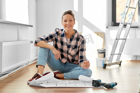 修理，人和房地产概念—妇女与蓝图和铅笔坐在地板在家里。妇女与蓝图坐在地板上在家里