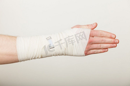 对摄影照片_骨折和脱位的概念。男人的手在白色绷带。对年轻人手掌手臂疼痛的有用药物。男性手缠绷带。