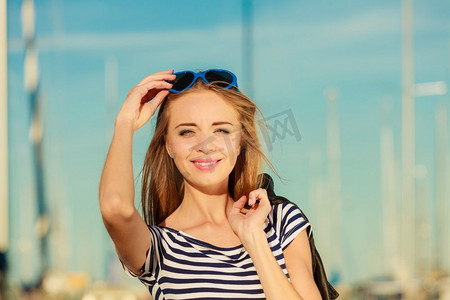 心形太阳镜摄影照片_夏季放松概念肖像女孩与蓝色心形太阳镜享受夏季微风室外在码头