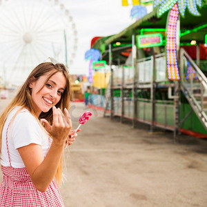 微笑的年轻女子拿着棒棒糖邀请某人来游乐园