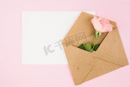白色空白卡棕色信封与玫瑰粉红色背景