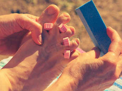 在海滩上度假期间做修脚的不可识别的妇女。女性用分离器打磨她的脚指甲。女子足疗户外
