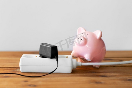 电力、能源危机与电力消费概念——小猪储蓄罐与电插座特写。存钱罐和电插座的特写