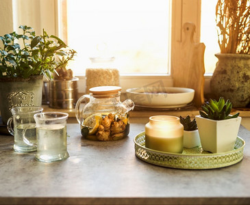 厨房水果背景摄影照片_舒适的早晨与柠檬和姜茶在厨房桌子与杯子、蜡烛和草药在窗口背景。热饮料。  前视图。