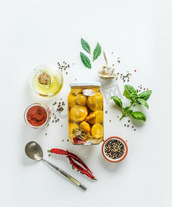 腌制的黄南瓜蔬菜在玻璃罐在白色背景与调味成分：香草，香料，油和匙。俯视图。