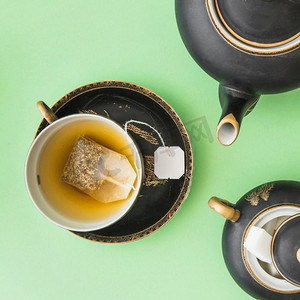 水果茶壶摄影照片_草药茶袋杯茶壶糖方块绿色背景