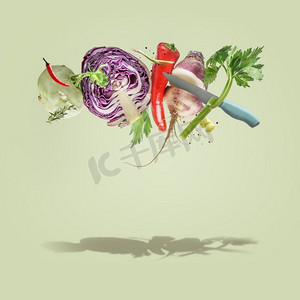 淡绿色背景摄影照片_创造性的食物悬浮概念与飞行各种五颜六色的蔬菜和刀在淡绿色背景。健康的生活方式