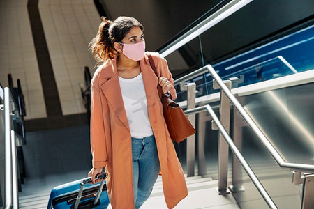 一名女子携带医用口罩行李在疫情期间爬机场楼梯