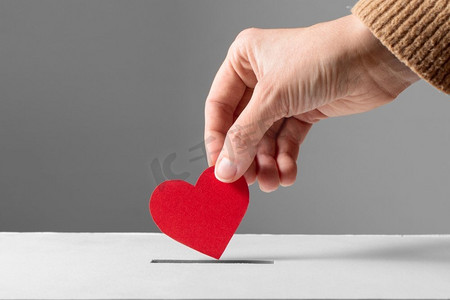 慈善、爱心、情人节&S日概念--将红心放进捐赠箱的特写。手把红心放进捐赠箱