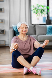 营业中摄影照片_运动、健身和健康的生活方式理念--快乐的老年女性在家中的运动垫上冥想。快乐的老年妇女在家中的垫子上冥想