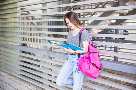 正在学习的学生摄影照片_女学生在墙边看课本