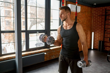 年轻强壮的男人在运动健身房用哑铃举重训练.美女健身运动