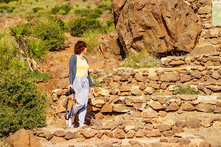 在西班牙，一位带着相机散步的女游客在户外拍摄地中海自然风光。一名在户外拍照的女游客