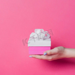 女性的手拿盒子与白色丝带蝴蝶结粉红色背景