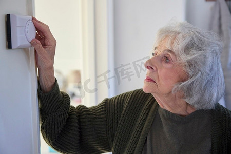能源危机中忧心忡忡的老妇人调低家里的中央供暖恒温器