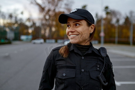 微笑的女警察站在街上看着旁边的肖像。以模糊的背景拍摄。微笑的女警察在街上的肖像