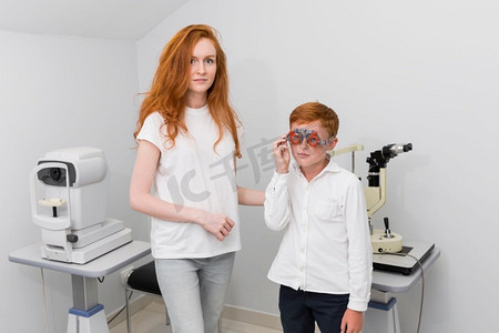 年轻的女配镜师在检查男孩患者的眼睛时看着摄像机