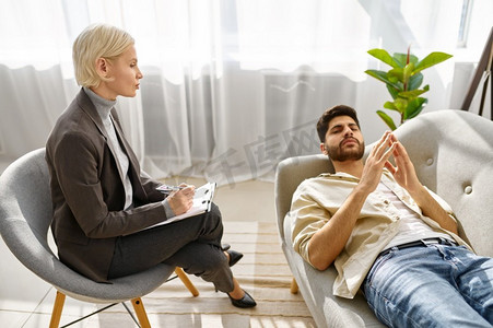 与躺在沙发上的年轻男子一起工作的女心理学家。盖伊试着放松地描述自己的感受。与男性坐在沙发上一起工作的女性心理学家