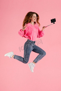 拿着照片摄影照片_拿着自拍杆跳起来的快乐女人肖像