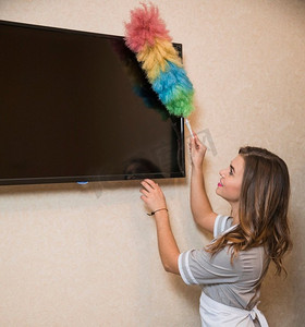 微笑的肖像年轻女子使用除尘器清洁的电视屏幕墙