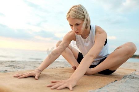 健身，运动，和健康的生活方式概念—妇女做瑜伽伸展姿势在海滩超过日落。妇女做瑜伽伸展姿势在海滩