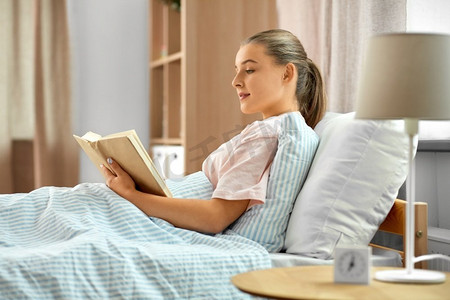 人、就寝时间与睡眠概念--微笑的女孩在家床上看书。微笑的女孩在家床上看书