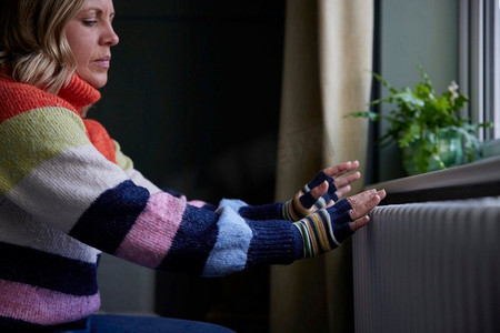 女人在家里戴手套暖手散热器期间生活能源危机