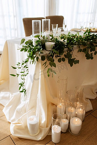 餐厅宴会厅的新人主席团用蜡烛和绿色植物装饰，紫藤悬挂在天花板上，