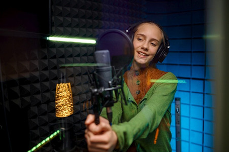 少年歌手艺人戴着耳机在录音棚用麦克风演唱录制新歌。少年歌手艺人演唱