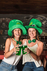圣帕特里克框摄影照片_笑的年轻妇女圣帕特里克斯帽子拥抱举行玻璃杯饮料酒吧柜台